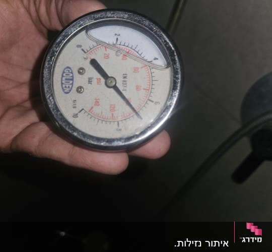 מד לחץ מים מוחזק ביד על רקע קיר אפור